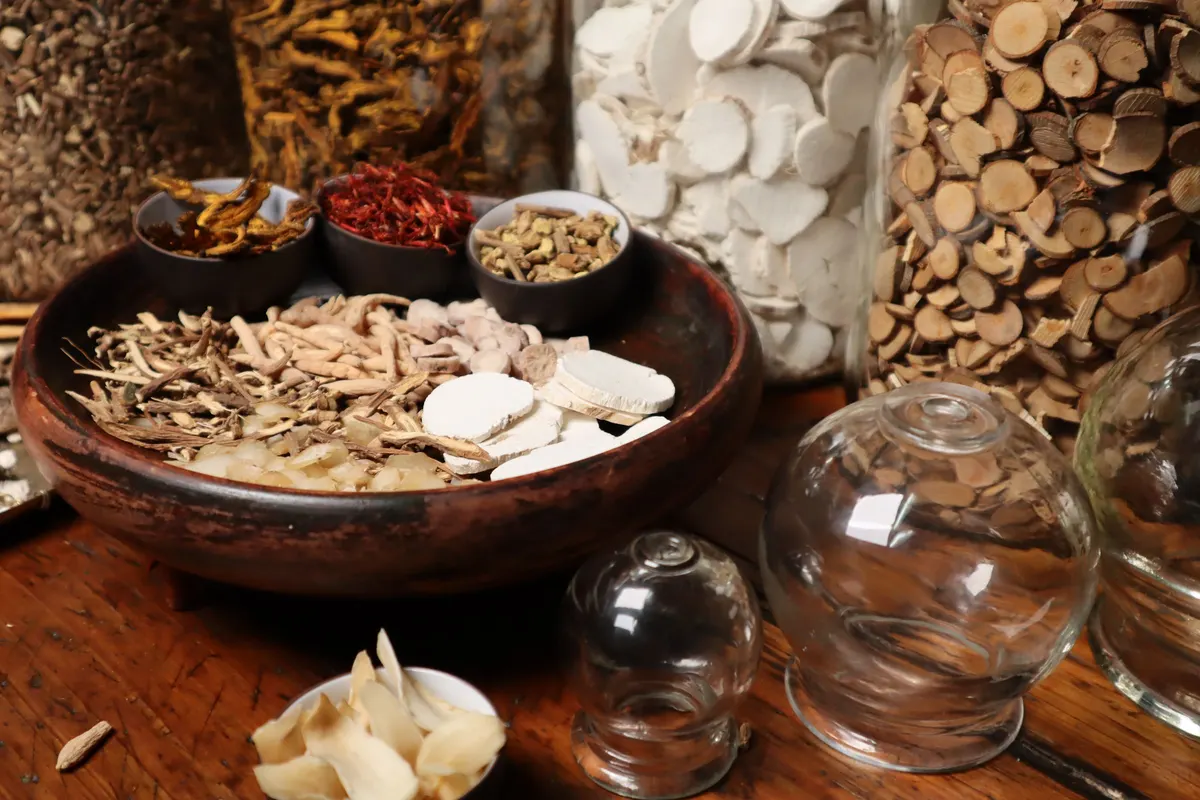 Dried roots, slices and seeds used in traditional Chinese herbal blends, in wooden bowls.