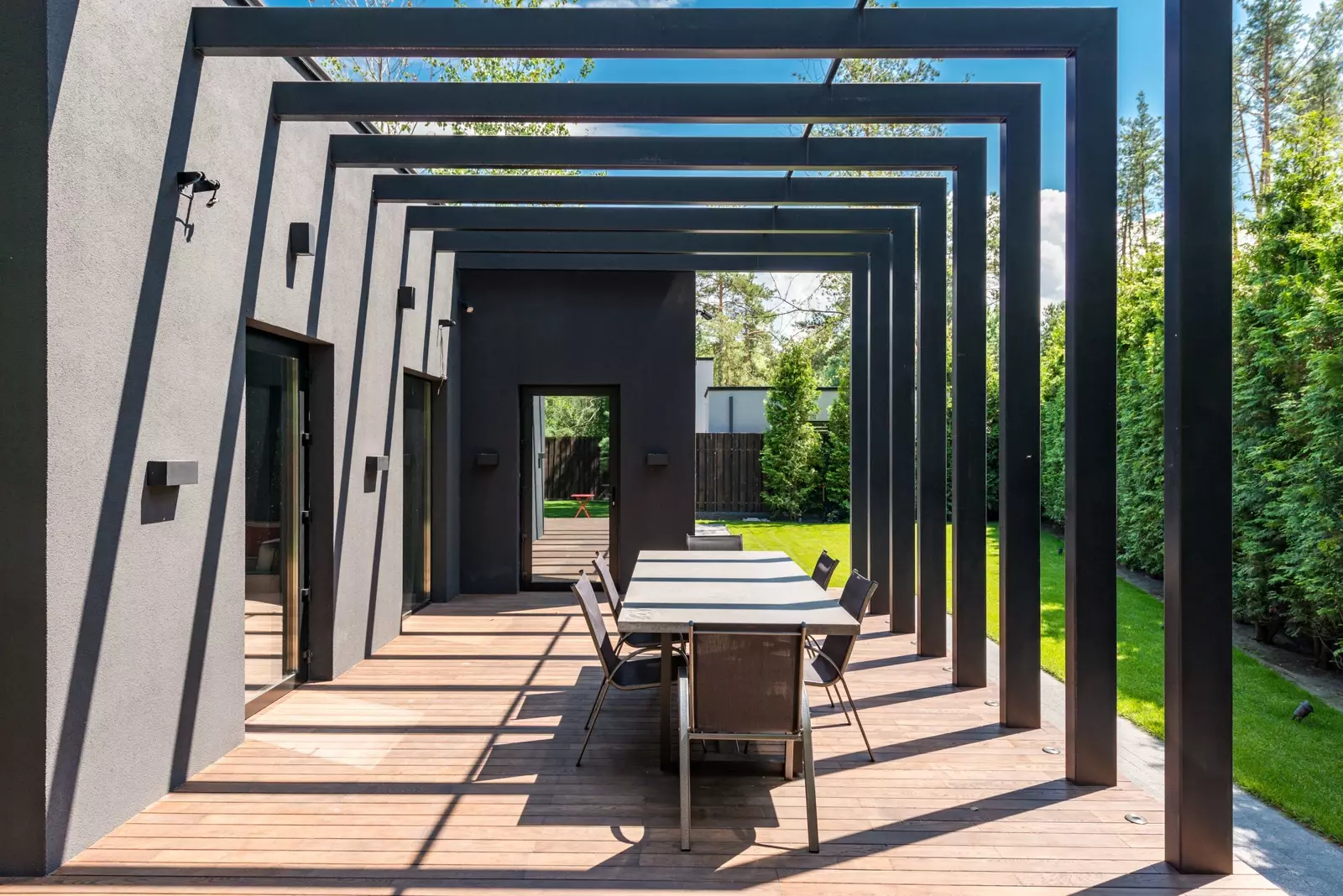 A modern pergola over a dining terrace beside a lawn