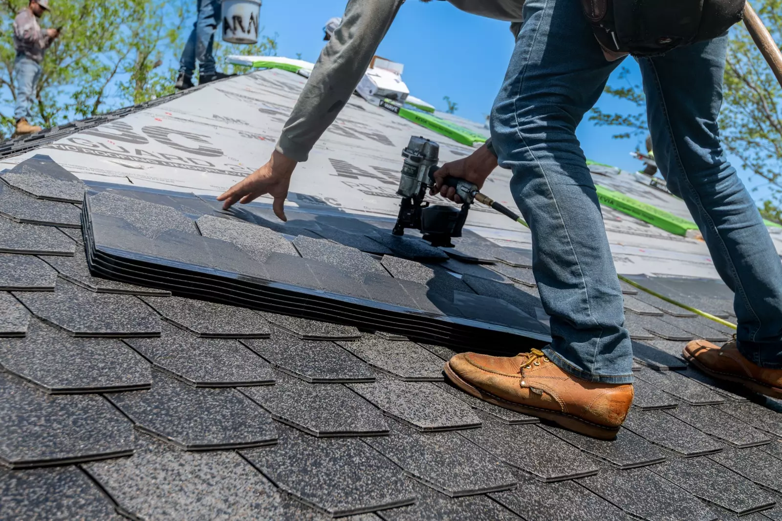 A roofer fastening new asphalt shingles on a home
